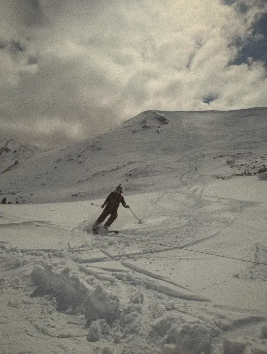 Skiing a powder turn below a snowy alpine ridge under heavy clouds