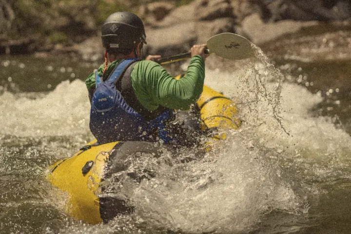 Paddling a yellow packraft through splashing whitewater